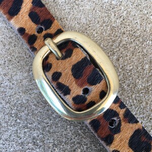 May include: A brown and black leopard print belt with a gold oval buckle.