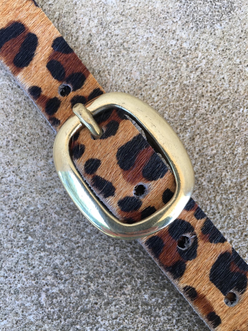 May include: A brown and black leopard print belt with a gold oval buckle.