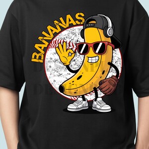 Peut inclure: T-shirt noir avec un personnage de banane de dessin animé portant des lunettes de soleil, une casquette de baseball et un casque. La banane fait un geste de la main "ok" et tient un gant de baseball. Le mot "BANANAS" est arqué au-dessus d'une balle de baseball.