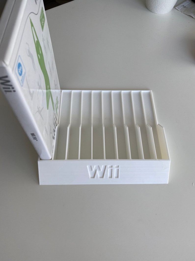May include: White plastic stand with slots for storing video game cases. The stand has the word "Wii" printed on the front.
