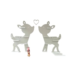 May include: Two gray deer-shaped shelves with white shelves and a heart-shaped cutout. The shelves are designed for wall mounting and have a whimsical, decorative appearance. A small figurine is placed between the shelves.