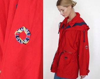 May include: Red hooded jacket with a blue and white logo that says "Marine Club" with a life preserver graphic. The jacket has a drawstring waist and two pockets.