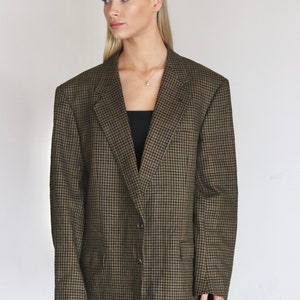 Op de afbeelding: Een bruin en zwart ruitjesjasje met een enkele knoopsluiting. Het jasje heeft een klassieke pasvorm en een licht oversized silhouet.