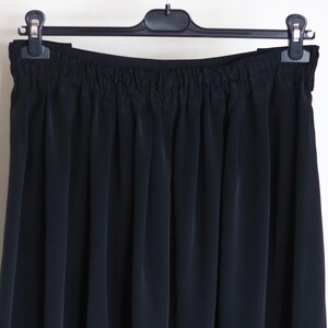 May include: A black skirt with a gathered waistband. The skirt is hanging on a black hanger.