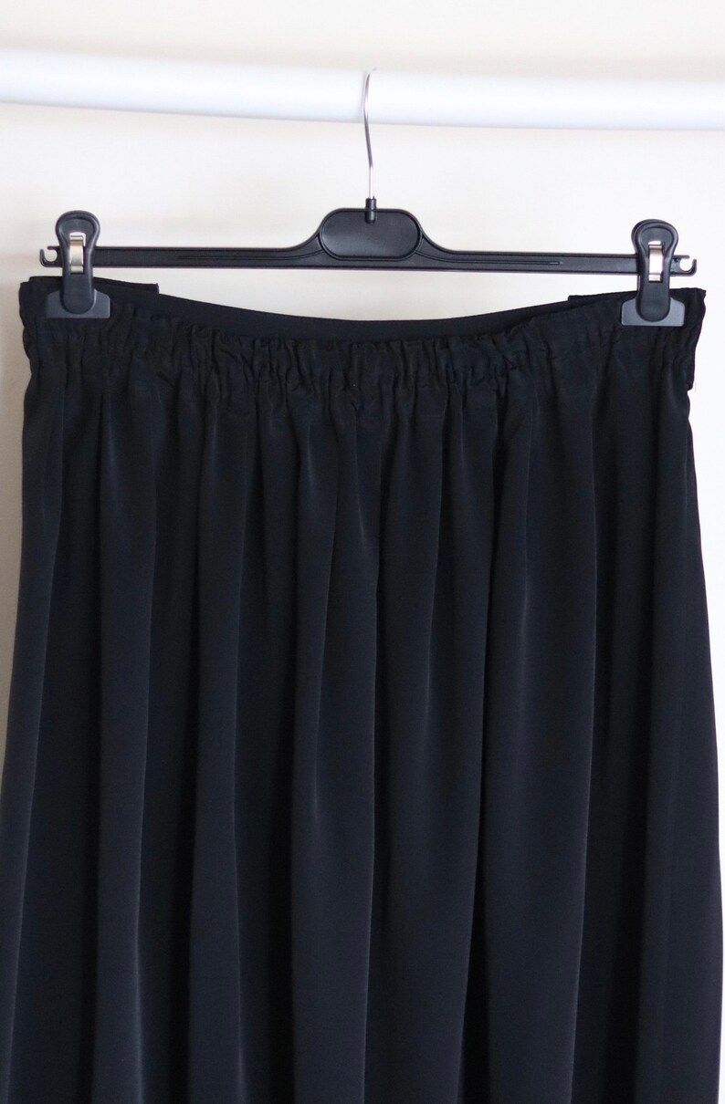 May include: A black skirt with a gathered waistband. The skirt is hanging on a black hanger.