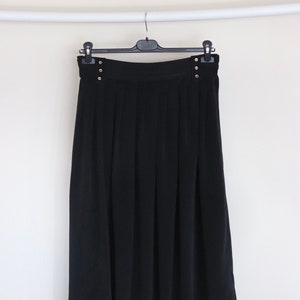 May include: A black pleated skirt with gold button accents. The skirt is hanging on a black hanger.