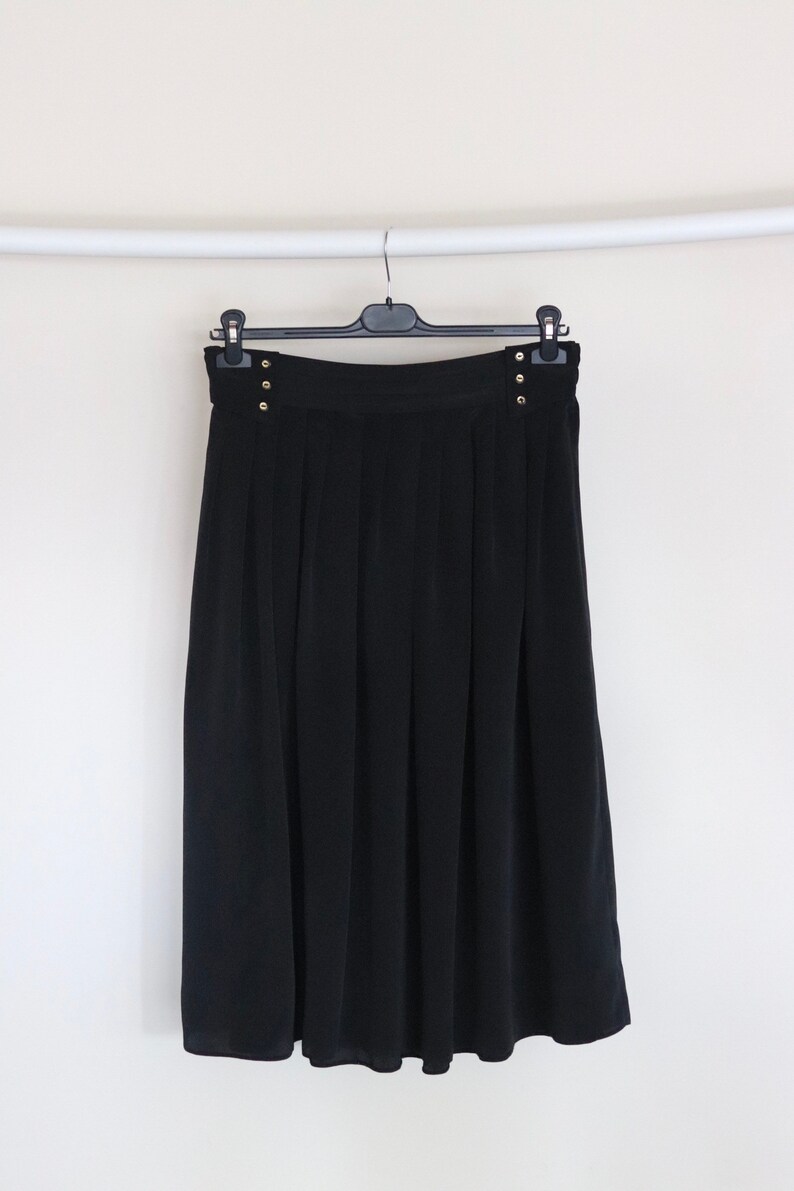 May include: A black pleated skirt with gold button accents. The skirt is hanging on a black hanger.