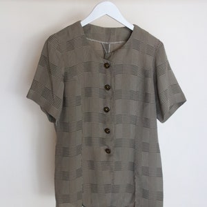 May include: A brown and black plaid button-up shirt with short sleeves. The shirt has a round neckline and is hanging on a white hanger.