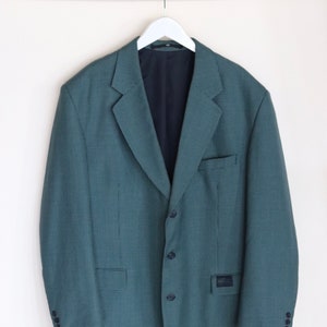 Op de afbeelding: Een tealblauwe blazer met een geruit patroon. De blazer heeft een enkele knoopsluiting en twee zakken.