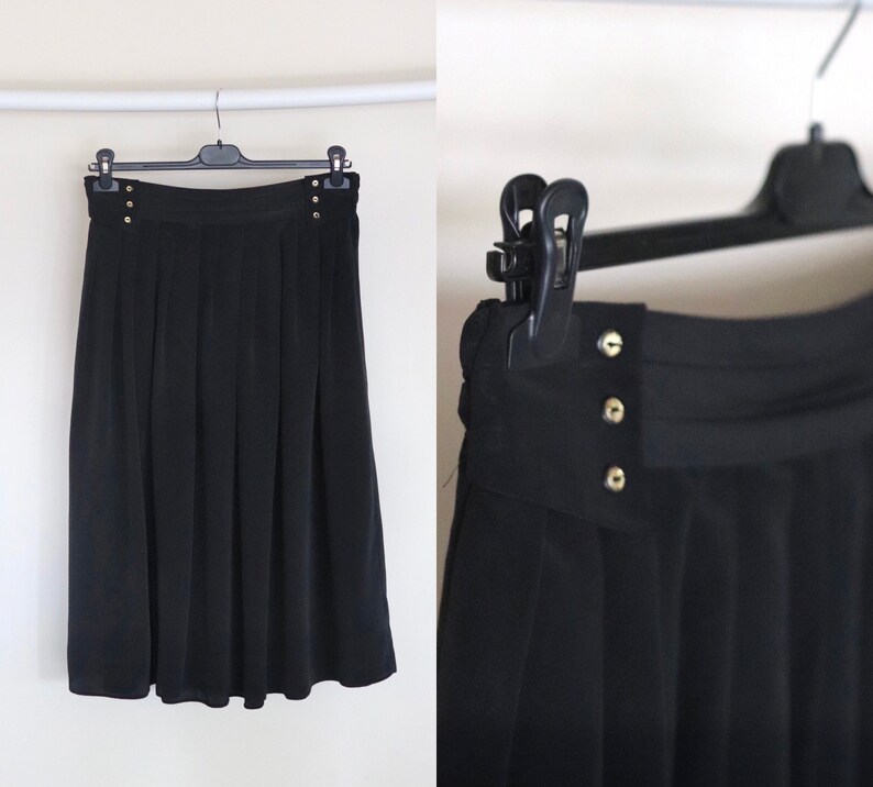 May include: A black pleated skirt with gold button accents. The skirt is knee-length and has a straight silhouette.
