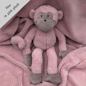May include: A pink plush monkey toy sitting on a pink fuzzy blanket. The monkey has a gray face and long arms and legs.