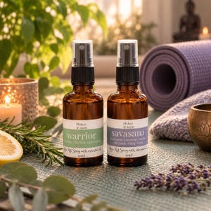 May include: Two amber glass spray bottles labelled Flicker & Scent, each containing 50ml of yoga mat spray. The left bottle is labelled warrior with rosemary, tea tree, and lemongrass, while the right bottle is labelled savasana with eucalyptus, lavender, orange, patchouli, and ylang ylang.