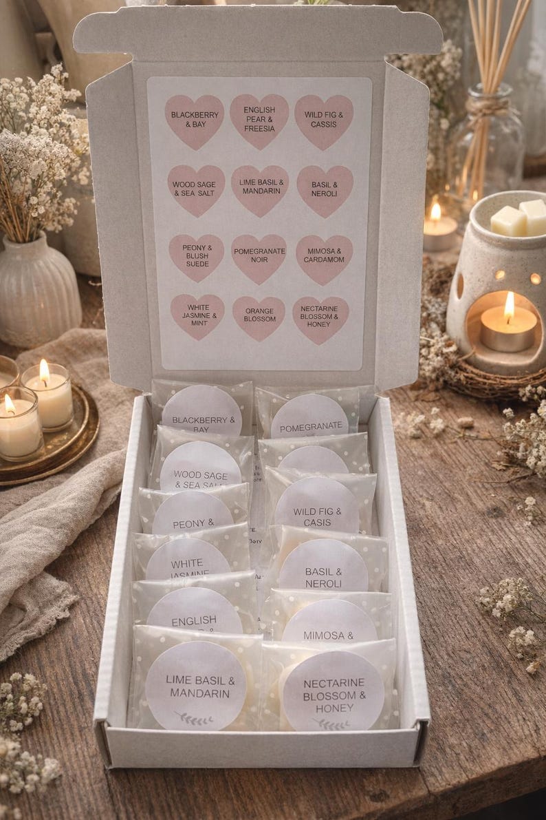 May include: A white box filled with scented wax melts, each labeled with a different fragrance name like "Blackberry & Bay" and "Lime Basil & Mandarin." The box is open, revealing the individual melts in clear packaging. The background includes candles and floral arrangements.
