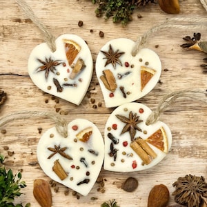 May include: Four heart-shaped wax melts with twine hangers, decorated with star anise, cinnamon sticks, cloves, and orange slices. The melts are arranged on a wooden surface with scattered spices and botanicals, creating a rustic, aromatic display.