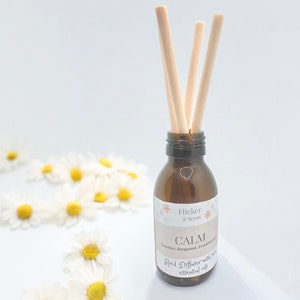 May include: A brown glass bottle with a label that reads "Flicker & Scent CALM Lavender, Bergamot, Frankincense Reed Diffuser with pure essential oils". The bottle has wooden sticks in it.