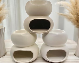 Könnte beinhalten: Drei Keramik-Duftöldiffusoren in verschiedenen Farben: Mokka, Creme und Weiß. Jeder Diffusor hat eine abgerundete, doppelte Birnenform mit einer hohlen Mitte.