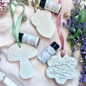 May include: Three ceramic diffuser ornaments with floral designs, each paired with a small bottle of essential oil. The oils are labelled "Relax", "Bloom", and "Spa Day".