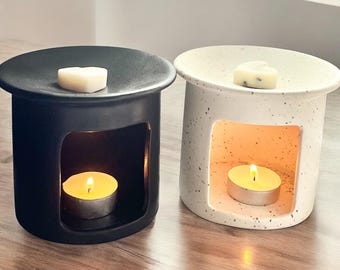 May include: Two ceramic wax warmers, one black and one white with speckles. Both have a heart-shaped wax melt on top and a tea light candle in the bottom.