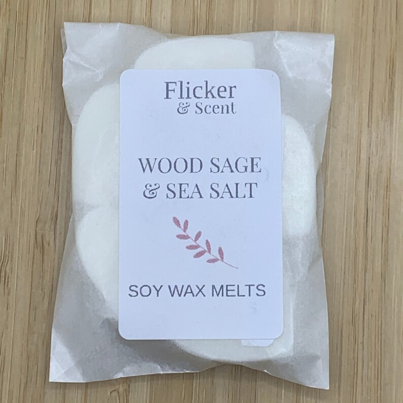 K&ouml;nnte beinhalten: Ein wei&szlig;er Papierbeutel mit einem Etikett, auf dem "Flicker & Scent" und "Wood Sage & Sea Salt Soy Wax Melts" steht.