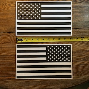 May include: Two black and white American flag decals. The flags are printed on white paper and have a black background. The stars are white and the stripes are black.