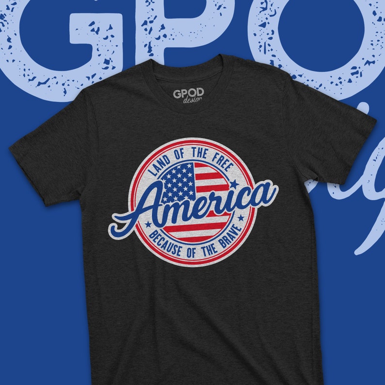 May include: A dark grey t-shirt with a vintage-style circular graphic featuring an American flag and the text "Land of the Free, America, Because of the Brave".