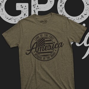 May include: A green t-shirt with a black circle graphic that says "Land of the Free, America, Because of the Brave" with a stylized American flag inside the circle.