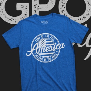 May include: A blue t-shirt with a white circle design featuring an American flag and the text "Land of the Free, America, Because of the Brave".