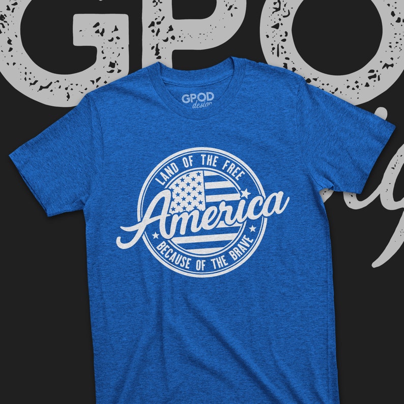 May include: A blue t-shirt with a white circle design featuring an American flag and the text "Land of the Free, America, Because of the Brave".