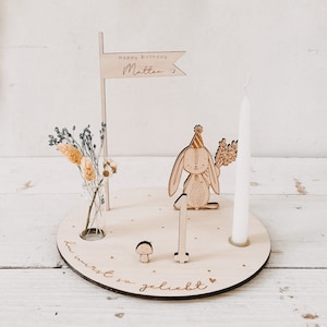 May include: Wooden birthday cake topper with a bunny holding a number one, a small mushroom, a vase with dried flowers, and a white candle. The topper has the text "Happy Birthday Matteo" and "Du wirst so geliebt".