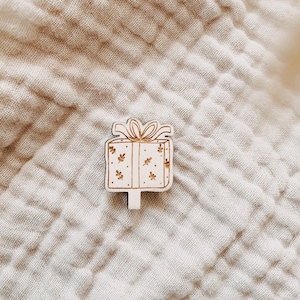 Könnte beinhalten: Ein Holz-Geschenkbox-Anhänger mit weißem Hintergrund und brauner Schleife. Die Box ist mit kleinen Blumenmustern verziert.