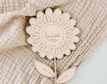 May include: A light-colored wooden flower cutout featuring a central stem with two leaves and a large circular bloom. The petals are engraved with various names, and the center contains the text: Luisa erzieherin mit, danke, dass du uns beim wachsen geholfen hast.
