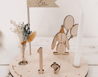 May include: Wooden first birthday cake topper with a bunny holding balloons, a candle, a number one, a flower, and a flag that says "Happy Birthday Ella".