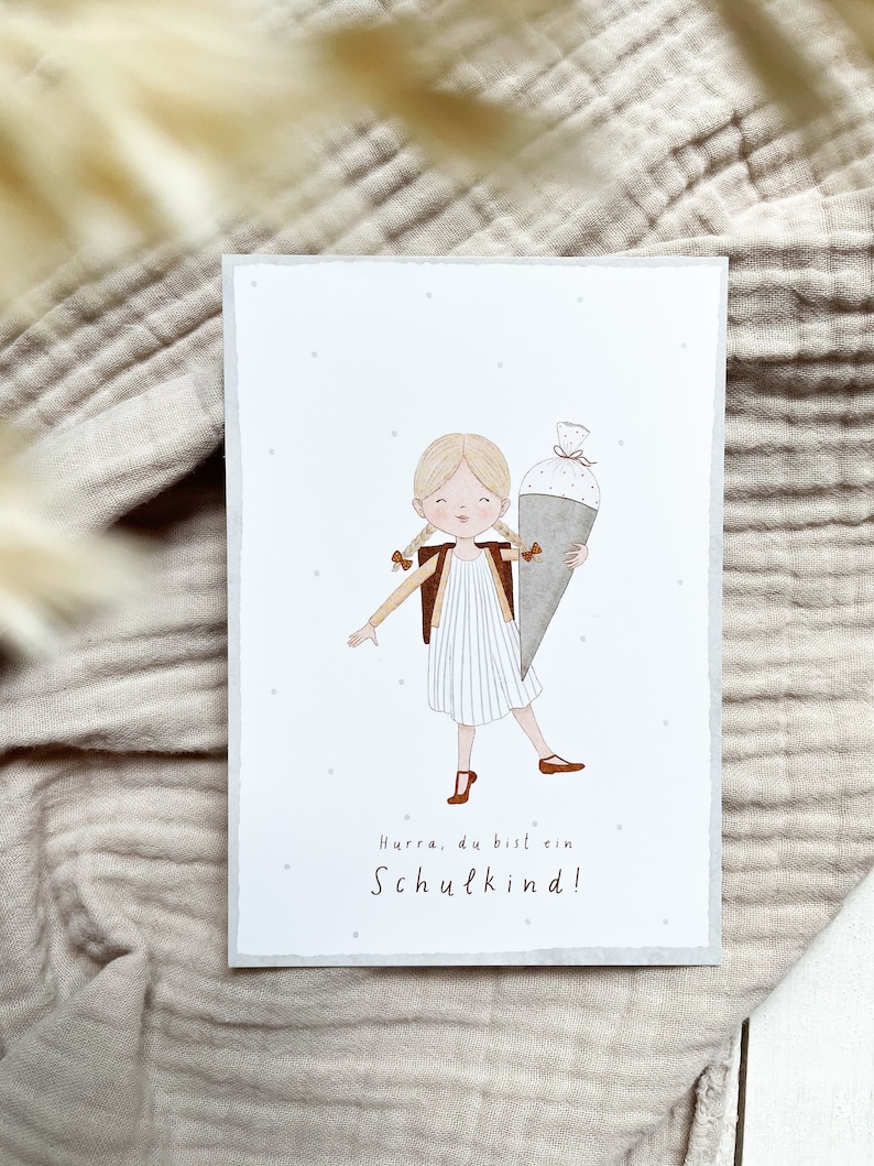 Postkarte mit Illustration eines lächelnden Schulkindes, das eine Schultüte trägt, mit dem Text ‘Hurra, du bist ein Schulkind!’ zur Einschulung.