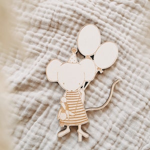 Könnte beinhalten: Holzschnitt einer Maus mit einer Partymütze, die Ballons hält. Die Maus hält eine kleinere Maus in ihren Armen.