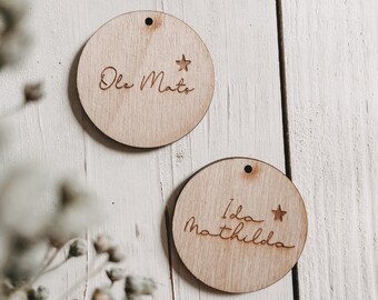 May include: Two round wooden ornaments with a star and a name engraved on each. The top ornament says "Ole Mats" and the bottom ornament says "Ida Mathilda".