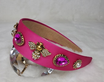 May include: A pink headband with gold and pearl embellishments, including a bee design and pink rhinestones.
