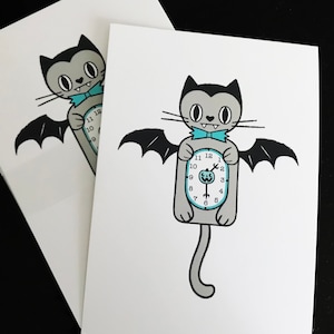 May include: Two white cards featuring a cartoon cat with bat wings and a clock body. The cat is gray with black accents, a blue bow tie, and a clock face showing the time. The cards are stacked on a black surface.