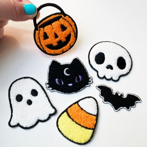 May include: Set of six Halloween-themed felt patches. The patches include a black cat, a ghost, a pumpkin, a skull, a bat, and a candy corn.