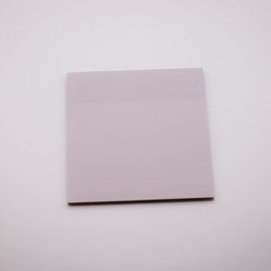 May include: A square, light purple sticky note pad. The top portion is slightly darker than the rest of the pad. The pad is on a white background.