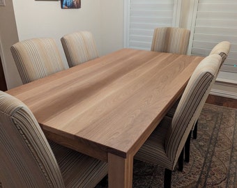 May include: A light wood dining table with a natural finish and six striped fabric chairs. The table is set in a dining room with a rug on the floor and a chandelier hanging above.