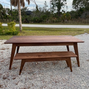 K&ouml;nnte beinhalten: Ein dunkelbraunes Holztisch- und Bankset im Mid-Century-Modern-Design. Tisch und Bank haben eine nat&uuml;rliche Holzoptik und abgeschr&auml;gte Beine.
