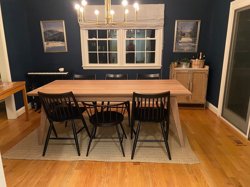 K&ouml;nnte beinhalten: Ein Esstisch aus Holz mit nat&uuml;rlicher Oberfl&auml;che und schwarzen St&uuml;hlen. Der Tisch steht in einem Esszimmer mit dunkelblauer Wand, einem Fenster mit wei&szlig;en Rahmen und einem Holzschrank.