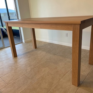 May include: A light brown wooden table with a rectangular top and four legs. The table is standing on a light brown tiled floor.