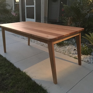 K&ouml;nnte beinhalten: Ein heller Holz-Esstisch mit rechteckiger Tischplatte und vier Beinen. Der Tisch ist aus massivem Holz und hat eine nat&uuml;rliche Oberfl&auml;che.