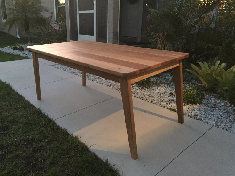 K&ouml;nnte beinhalten: Ein heller Holz-Esstisch mit rechteckiger Tischplatte und vier Beinen. Der Tisch ist aus massivem Holz und hat eine nat&uuml;rliche Oberfl&auml;che.