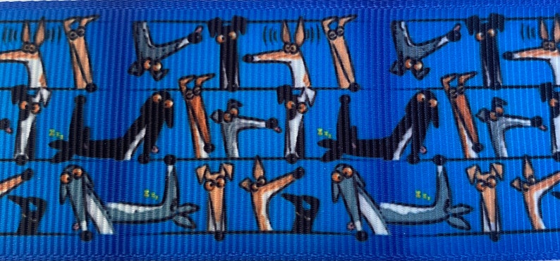 Op de afbeelding: Blauw patroonlint met een herhalend ontwerp van cartoonhonden in verschillende poses. De honden zijn in tinten bruin, grijs en zwart, waarvan sommige lijken te slapen. Het lint is geschikt voor knutselen of huisdieraccessoires.