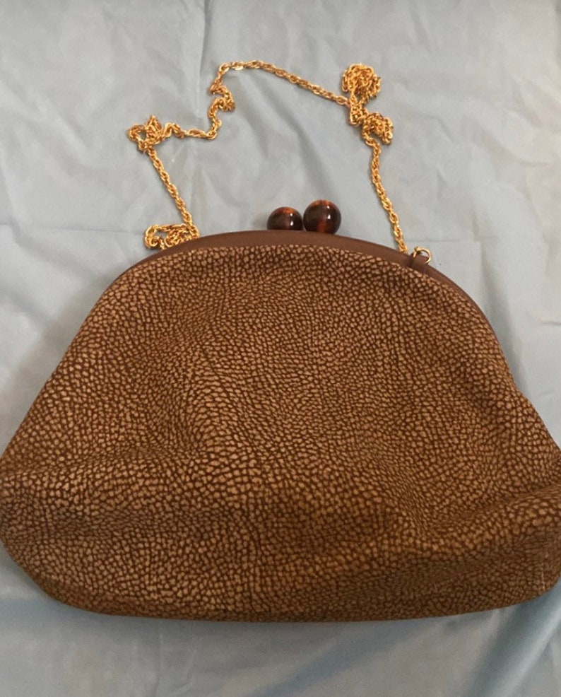 Puede incluir: Un bolso de mano de cuero marr&oacute;n con una correa de cadena dorada y dos detalles de carey marr&oacute;n.