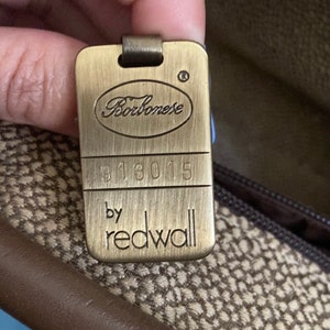 Puede incluir: Una etiqueta de metal de color dorado con el texto "Borbonese" en letra cursiva, el n&uacute;mero "913015" y el texto "by redwall".