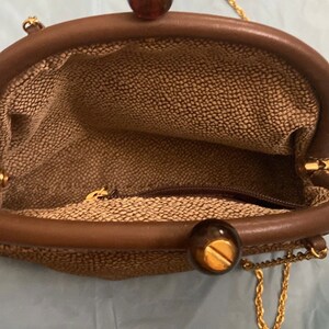 Puede incluir: Un bolso tejido marr&oacute;n con una correa de cadena dorada y dos cierres redondos marrones y dorados.