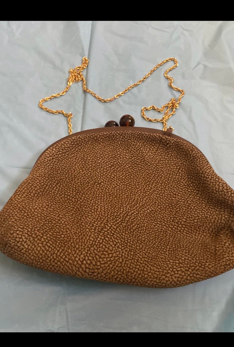 Puede incluir: Un bolso de mano marr&oacute;n texturizado con una correa de cadena dorada y dos cierres de pl&aacute;stico marr&oacute;n.